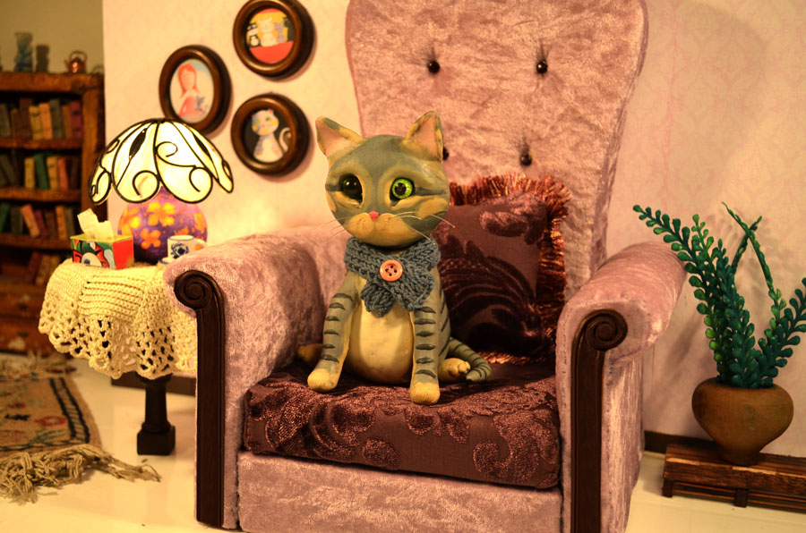 Stop Motion Puppe als Katze sitzt auf einem vornehmen Sessel in einem Miniatur Wohnzimmer Filmset