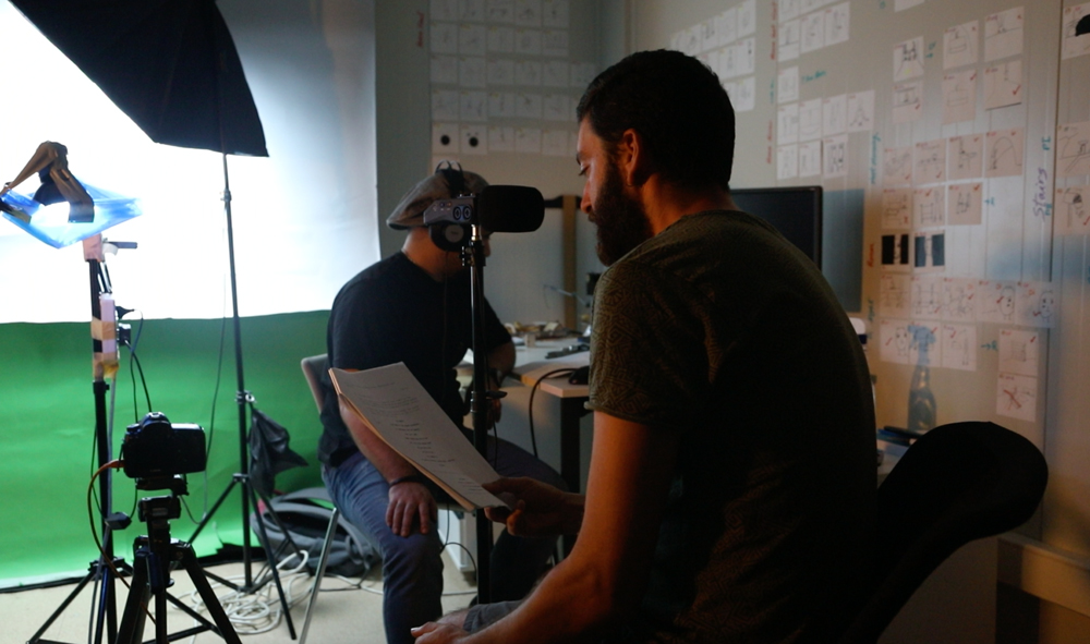 Der Direktor und Voice Actor nehmen im Studio die Stimme für den Charakter der Animation Mr. Rabbit's Doll auf, im Hintergrund sehen wir einen Greenscreen, Lampen und das Storyboard an der Wand.